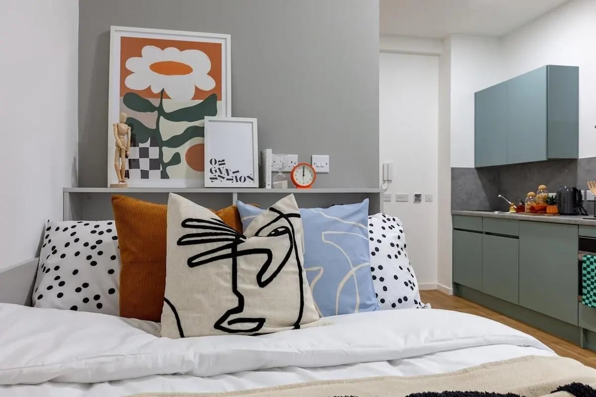 Bed with art pillows and kitchen area bedroom at The Waterways Nottingham in Nottingham Student Accommodation