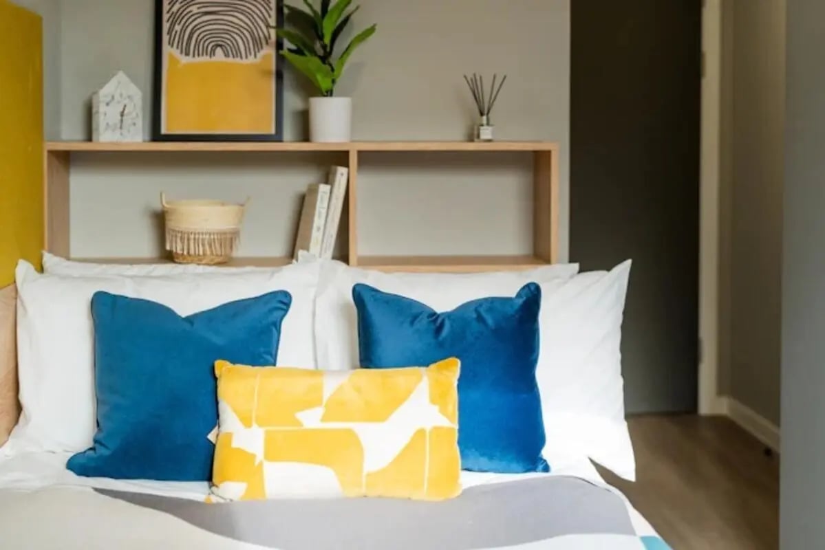 Bed with blue and yellow pillows shelf bedroom at Zinc Quarter in Bristol Student Accommodation