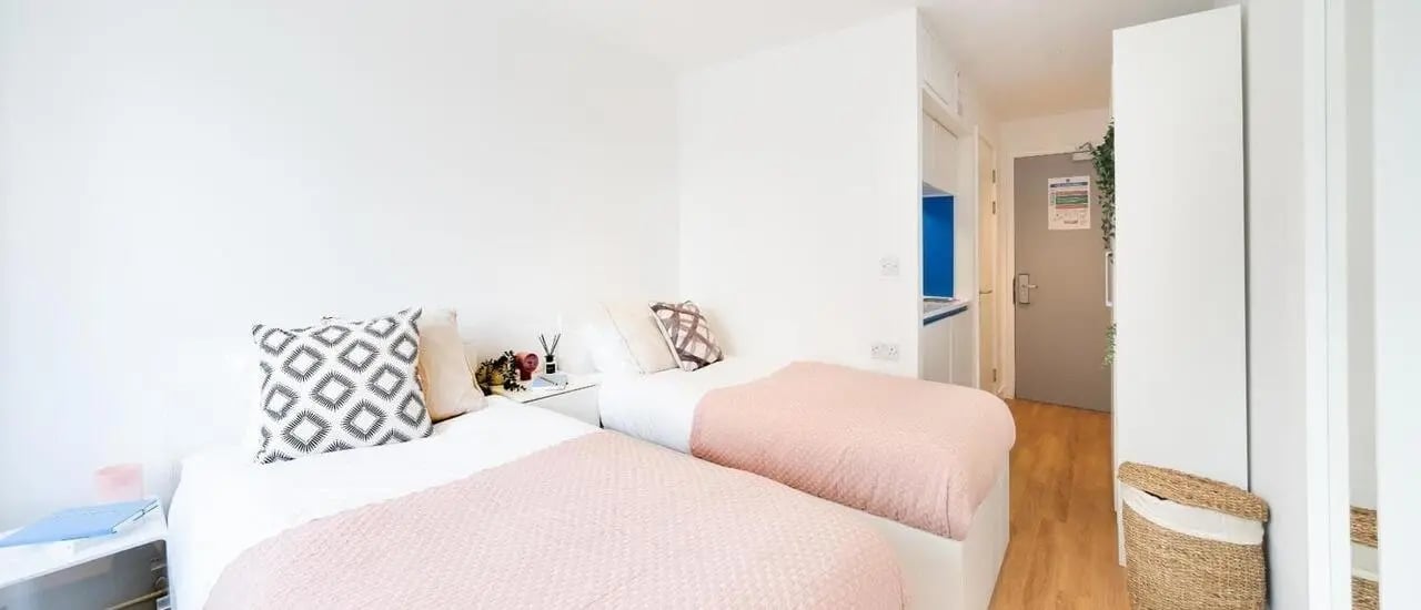 Two beds pink blankets patterned pillows and bedside table Bedroom at Chapter Aldgate in London Student Accommodation