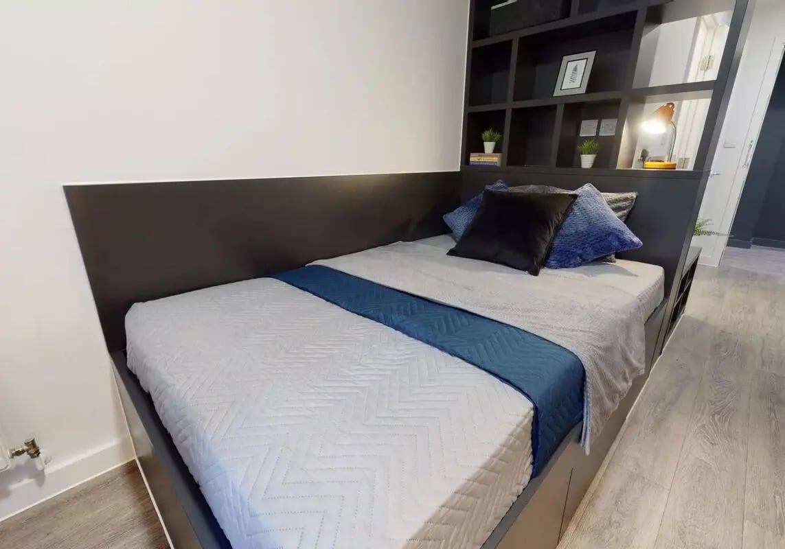 Bed with blue blanket black pillows and shelves bedroom at iQ Shoreditch in London Student Accommodation