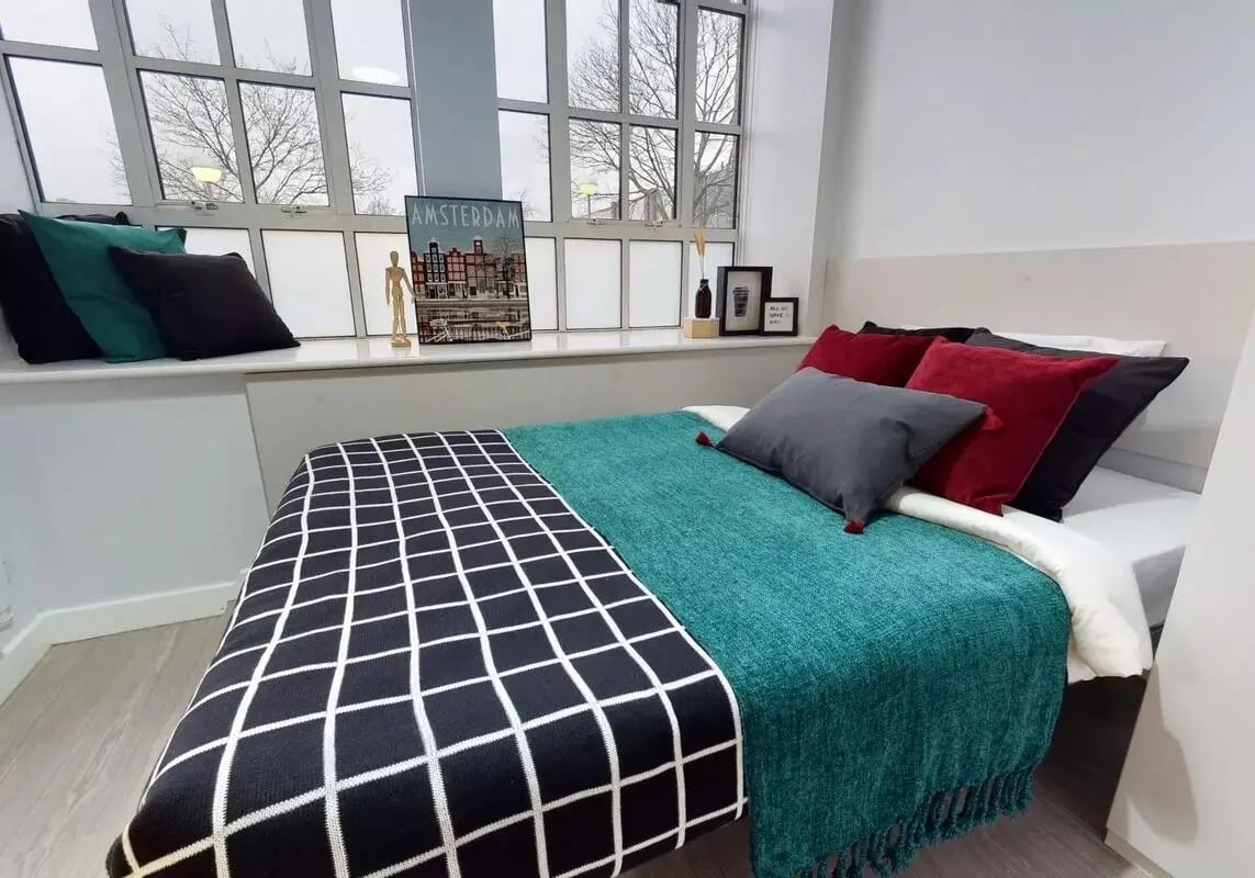 Bed with pillows Amsterdam artwork and window Bedroom at iQ Studios 51 in Birmingham Student Accommodation