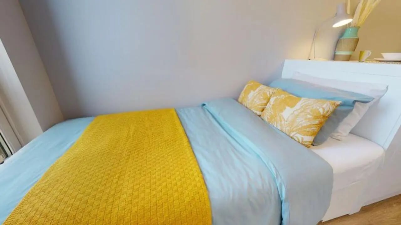 Bed with blue bedding yellow throw patterned pillows Bedroom at iQ East Court in London Student Accommodation
