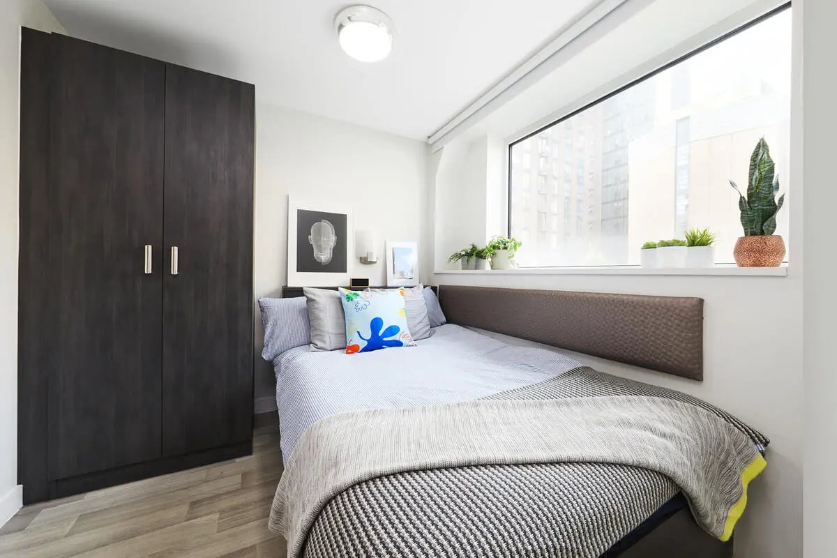 Dark wardrobe bed with pillows artwork plants bedroom at Collegiate Tower in Bristol Student Accommodation