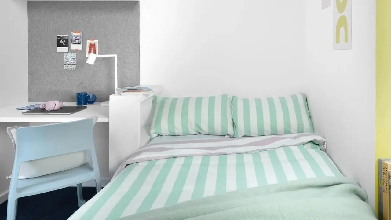 Bed with striped bedding desk and chair bedroom at Scape Mile End in London Student Accommodation