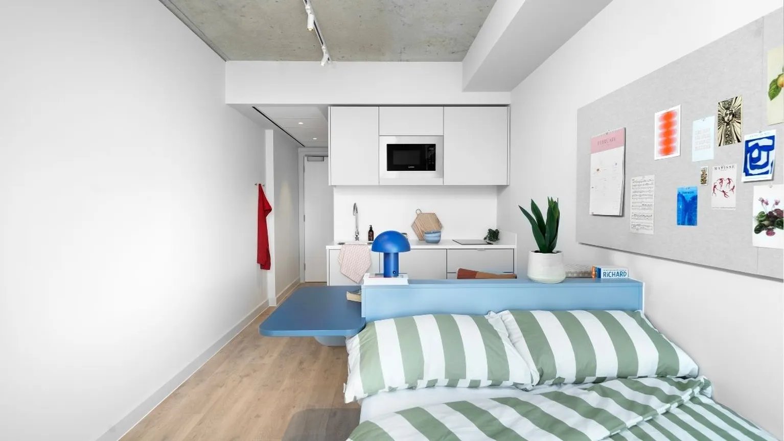 Bed with green striped duvet and kitchen area bedroom at Scape Hammersmith in London Student Accommodation