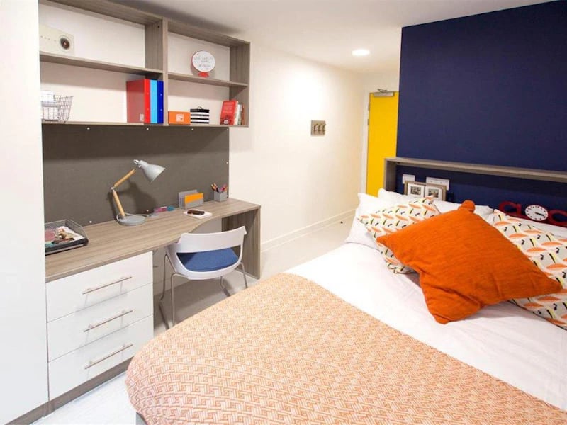 Desk lamp shelves bed and orange pillow bedroom at Foundry Courtyard in Glasgow Student Accommodation