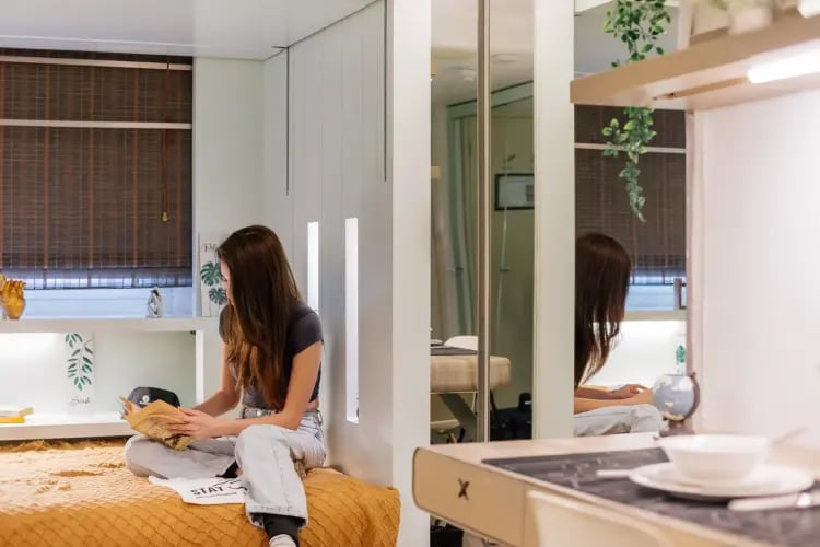 Woman reading on bed with compact kitchen area Bedroom at The Stay Club - Camden in London Student Accommodation