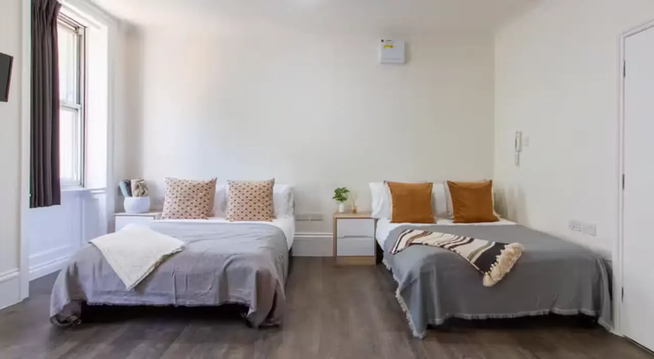 Two beds with patterned pillows and grey blankets bedroom at Bloomsbury Janet Poole House in London Student Accommodation