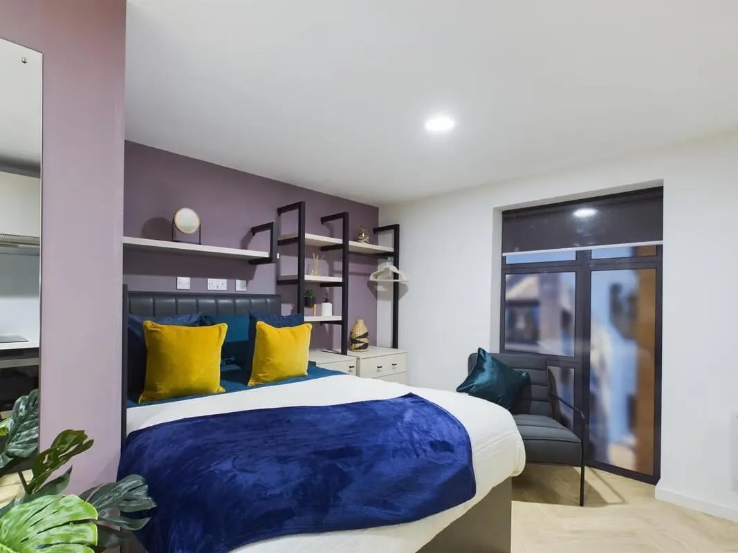 Bed with yellow pillows dark throw chair window bedroom at Arcadian in Nottingham Student Accommodation