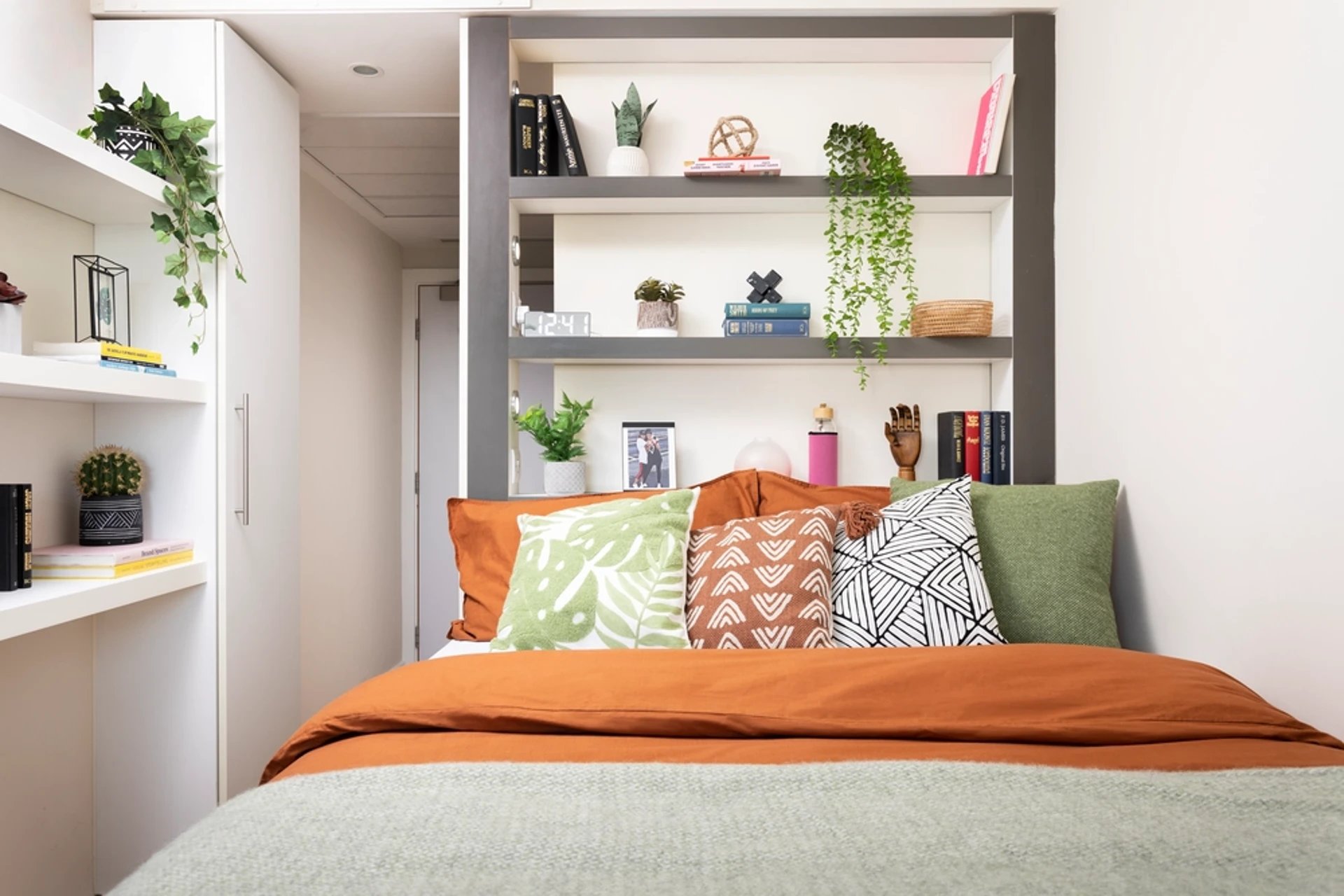 Bed with orange linen decorative pillows and shelves bedroom at Bridgewater Heights in Manchester Student Accommodation