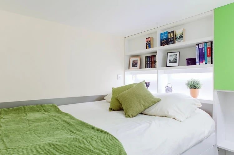 Bed with green blanket and bookshelves bedroom at Cathedral Park in Bristol Student Accommodation