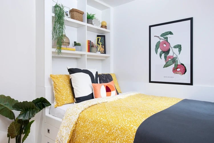 Bed with yellow bedding shelving with plants and artwork bedroom at Adam Street Gardens in Cardiff Student Accommodation