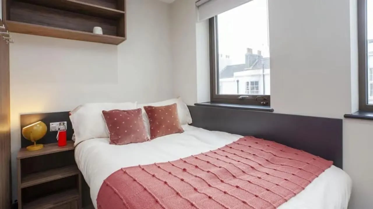 Bed with pink throw bedside table lamp and shelf Bedroom at Crown House Brighton in Brighton Student Accommodation