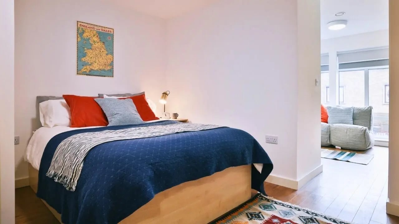 Bed with red pillows desk lamp and map bedroom at Pavilion Court in Canterbury Student Accommodation