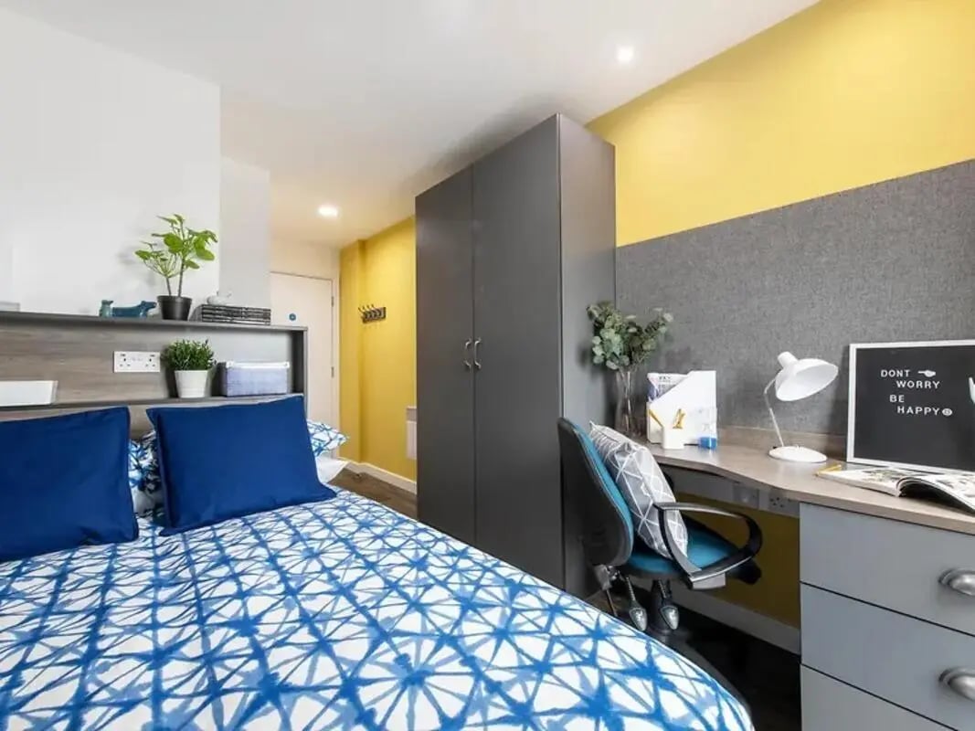 Bed with blue pillows grey wardrobe desk with lamp bedroom at Yugo Bentley House in Birmingham Student Accommodation