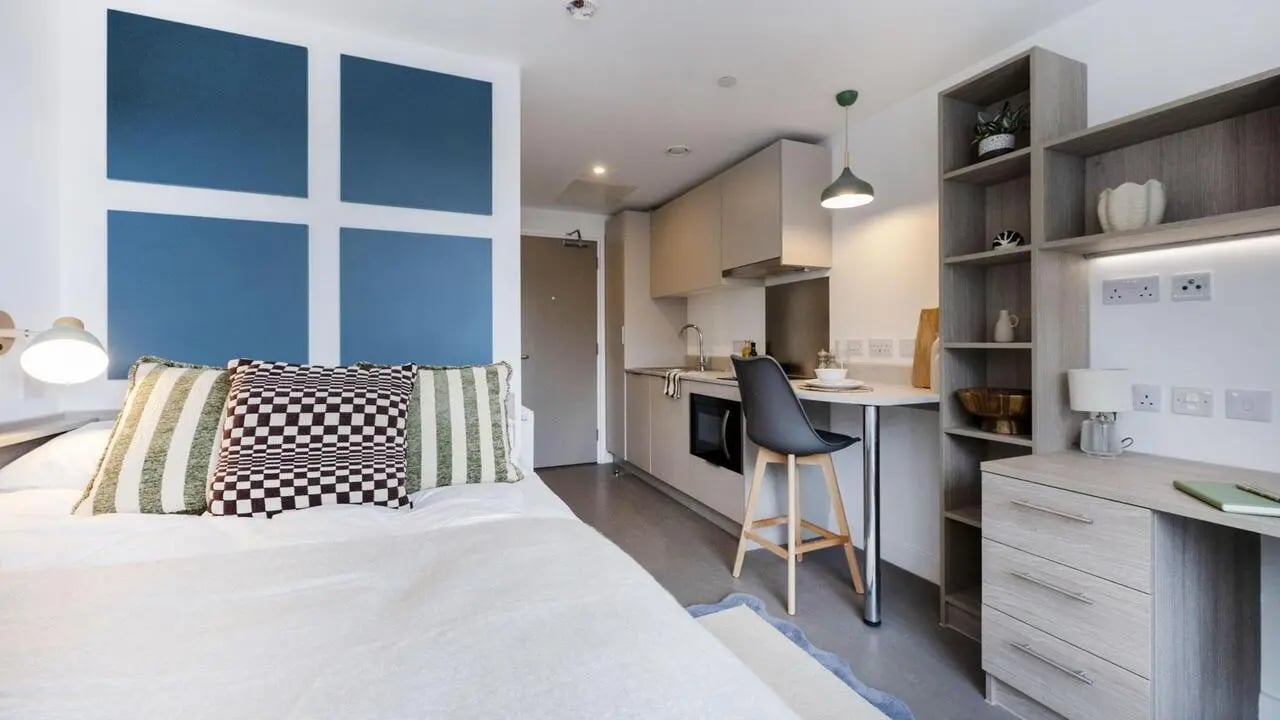 Bed with pillows kitchen counter and desk Student room at Timber Yard in Bristol Student Accommodation