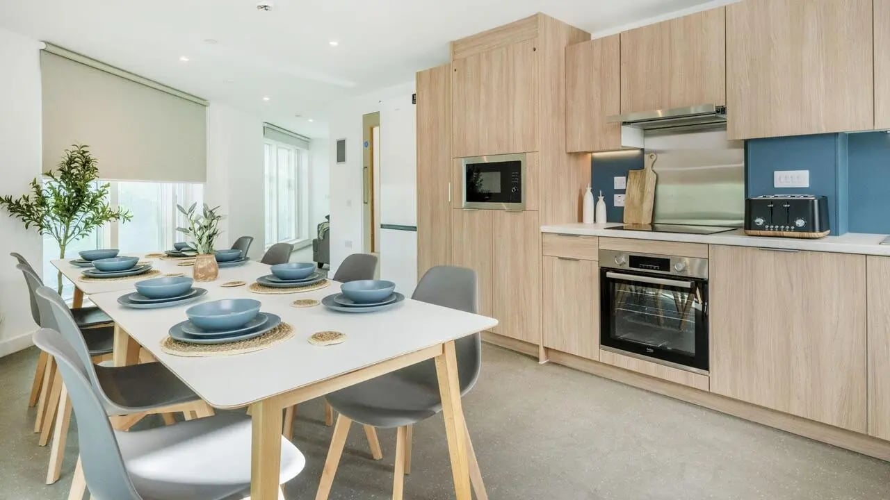 Dining table with place settings and modern kitchen area. at Timber Yard in Bristol Student Accommodation