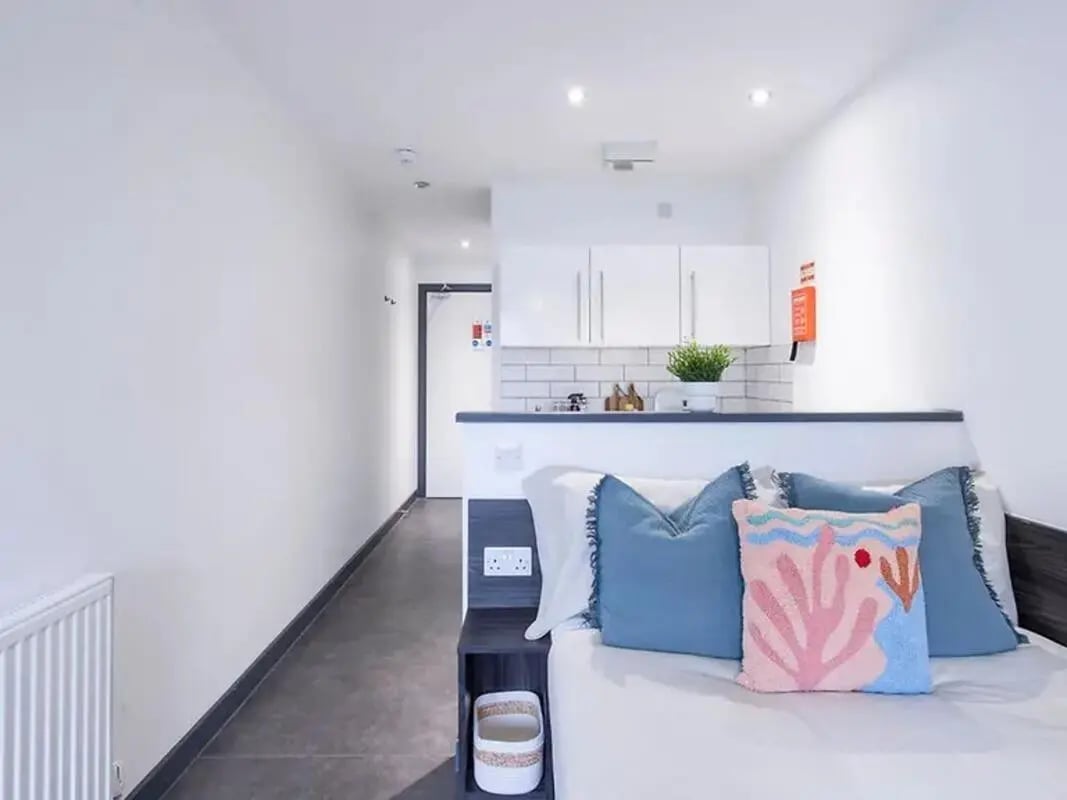 Bed with blue pillows and kitchen area Studio at The Foundry Newcastle in Newcastle Upon Tyne Student Accommodation