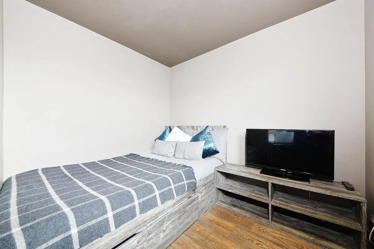 Bed with grey blanket and blue pillows tv bedroom at Marketgait Apartments in Dundee Student Accommodation