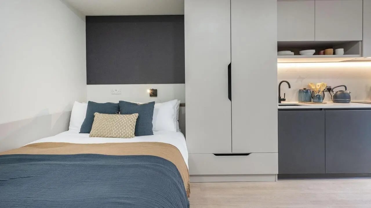 Bed with pillows and modern kitchen area living room at Broadway Studios in Glasgow Student Accommodation