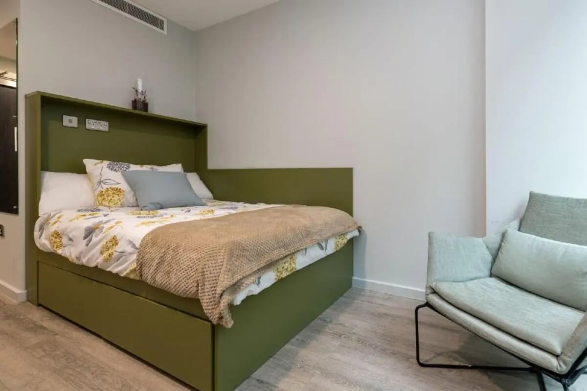Bed with floral sheets and green headboard armchair bedroom at Flora Building - Hoxton in London Student Accommodation