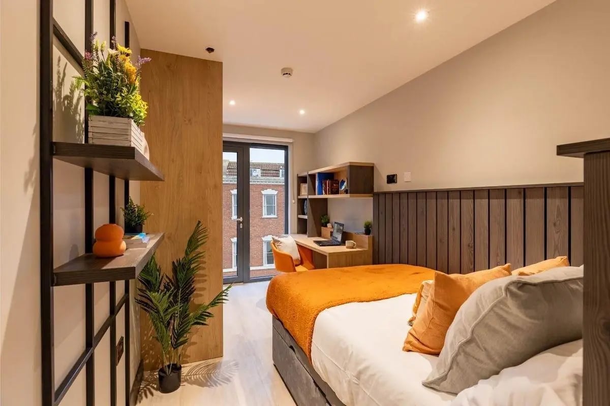 Bed with orange throw desk plants shelving bedroom at The Port On The Square in Bristol Student Accommodation
