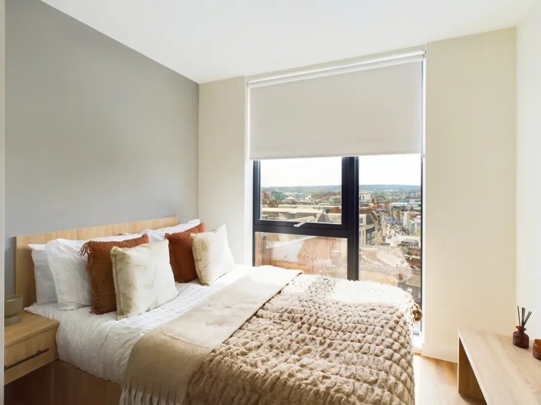 Bed with cushions blinds and city view bedroom at Straits Aire in Leeds Student Accommodation