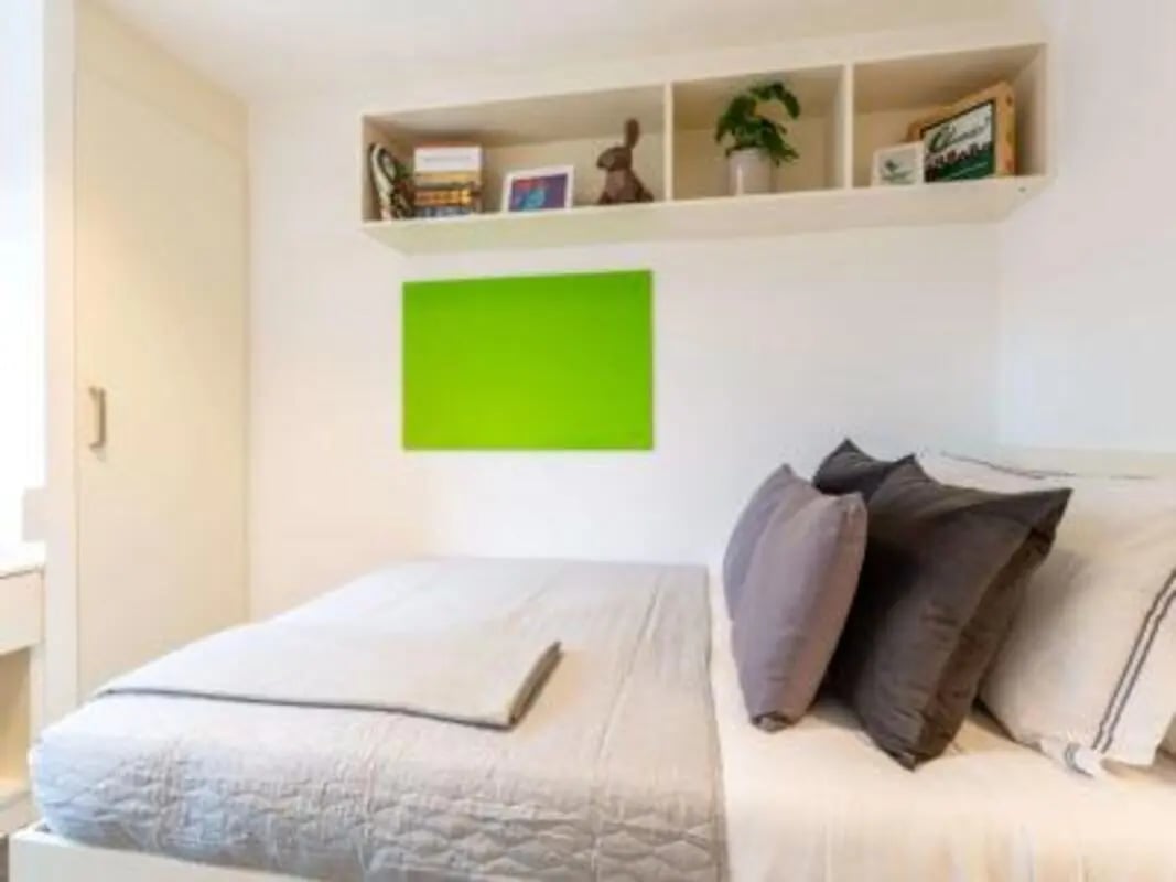 Bed with pillows wardrobe shelf and green art bedroom at Harbour Court in Bristol Student Accommodation
