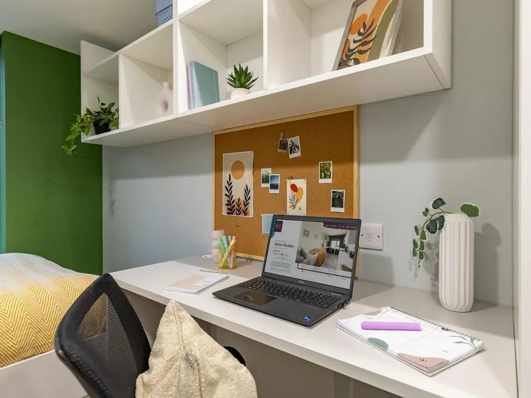 Desk with laptop corkboard shelves and bedding study area at Venue Studios in London Student Accommodation