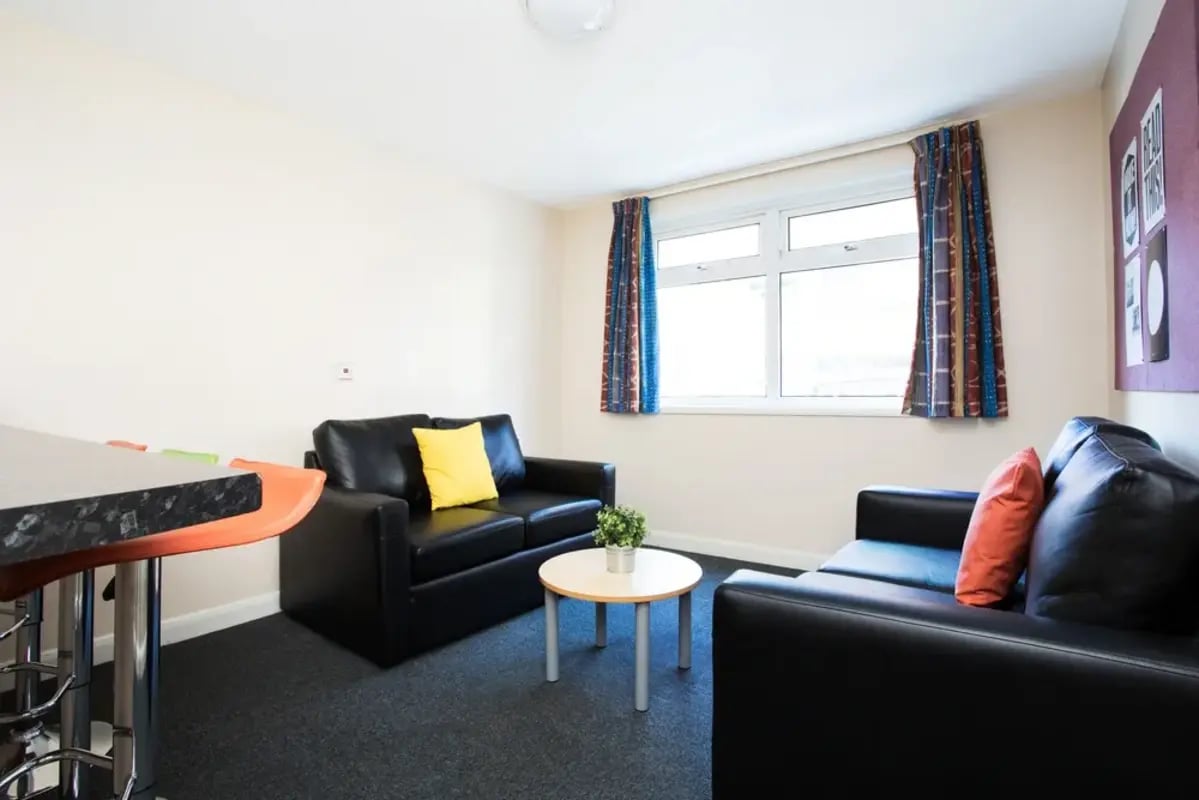 Black sofas yellow and orange pillows living room at St Martins House in Leicester Student Accommodation