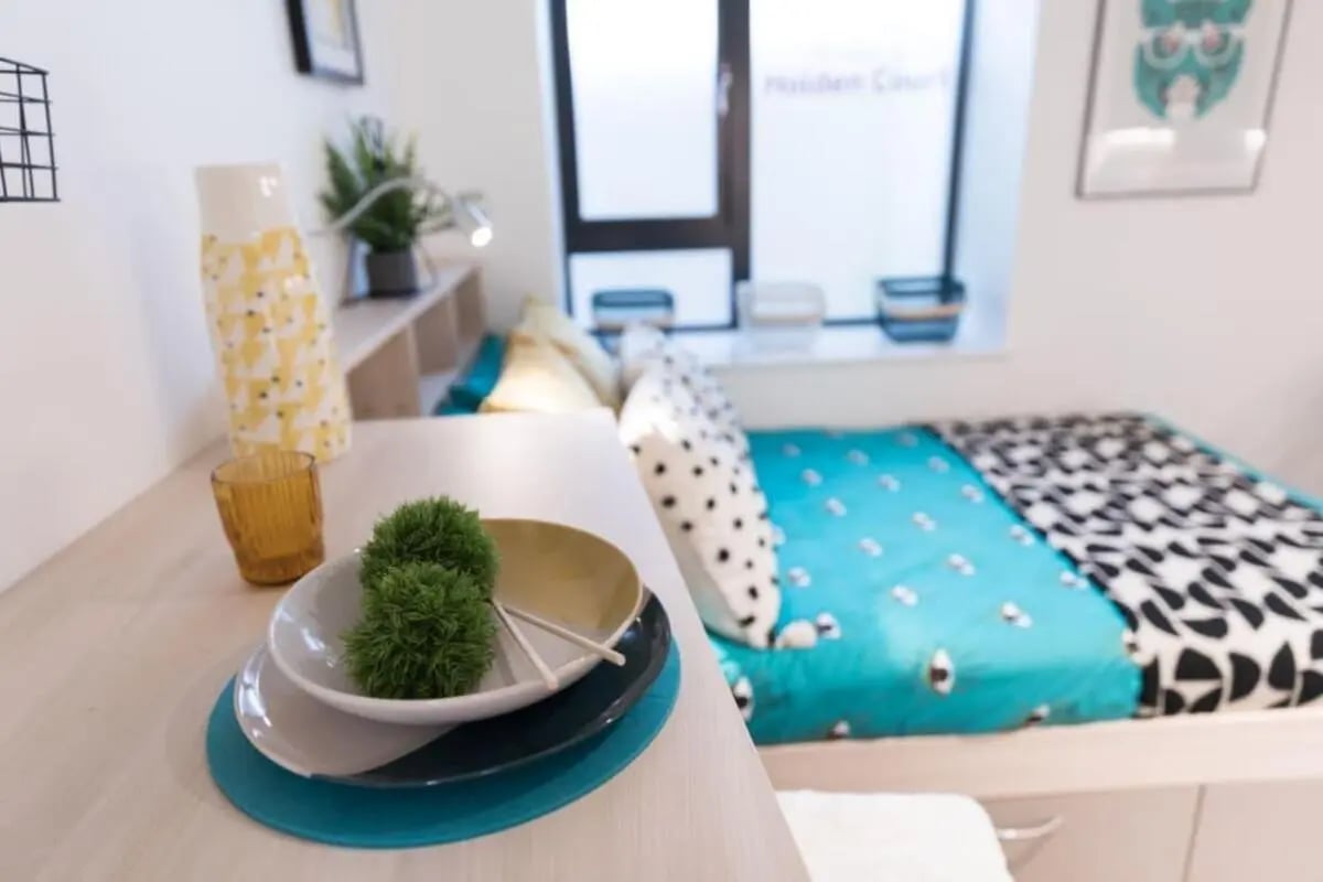 Bed with colorful bedding and desk with plates bedroom at Holden Court in Brighton Student Accommodation