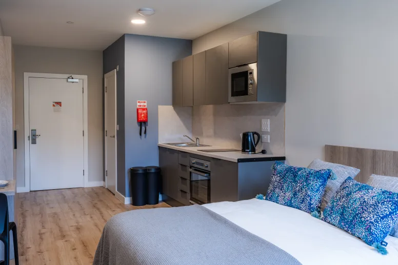 Bed with kitchen area and door studio apartment at Boutique Student Living Swansea in Swansea Student Accommodation